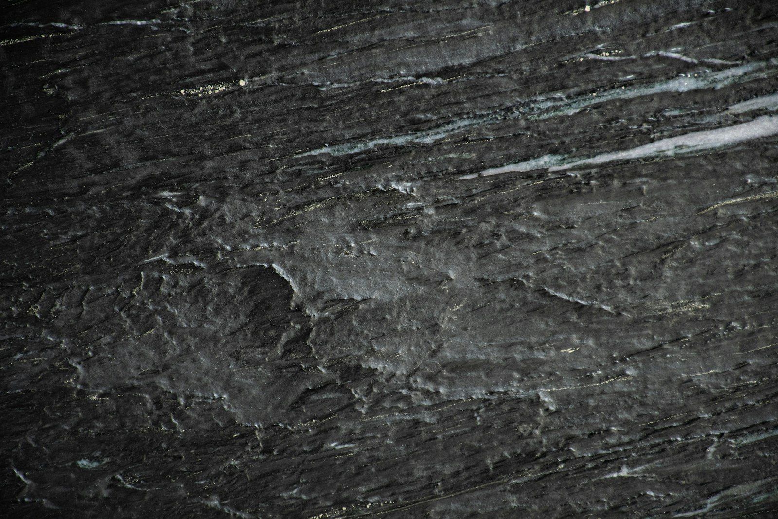 Near-black marble shot close, faint mineral veins running through the dark surface.